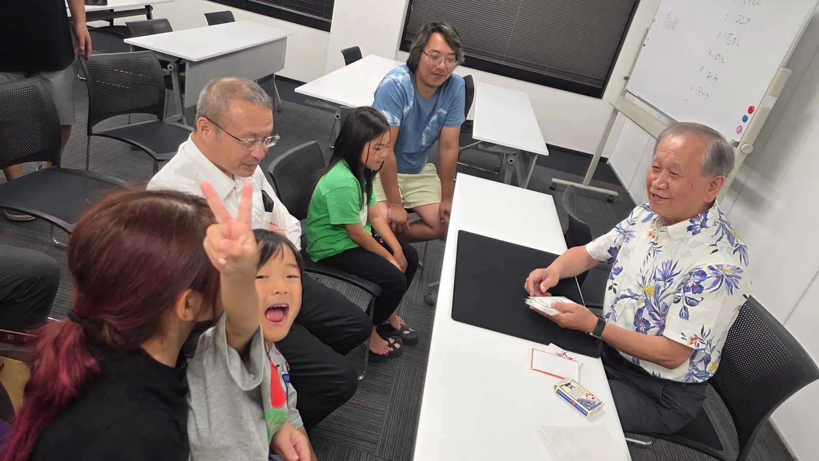 富山のマジックサークルを見学したご家族の夜|まじっぱ8月24日レポート 3 花柄のアロハシャツで座ってカードマジックを演じるベテランメンバーと囲むまじっぱの仲間たち|富山マジックサークル