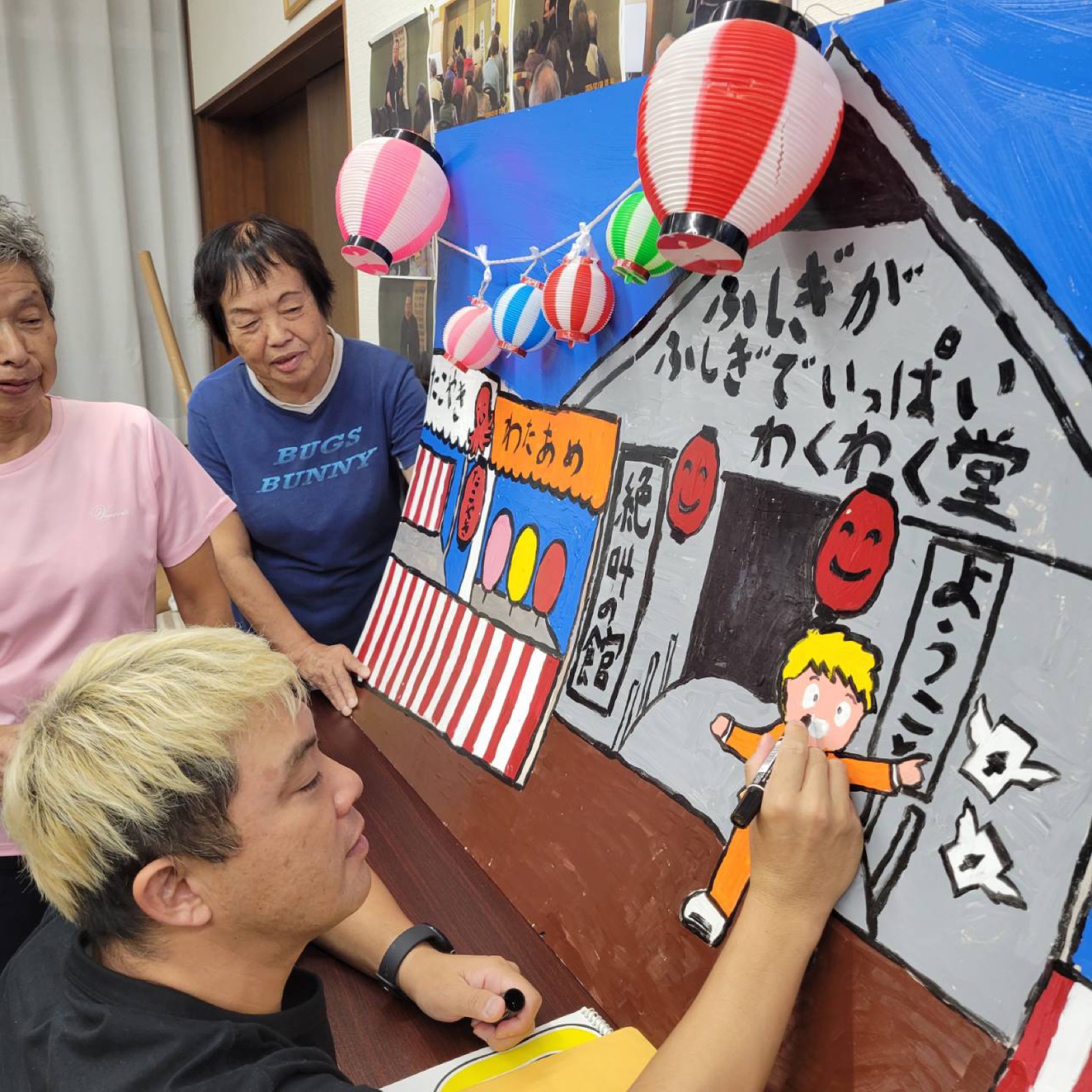 愛の劇団の縁日背景幕にダルマ式の目入れを行うコンプレッサー