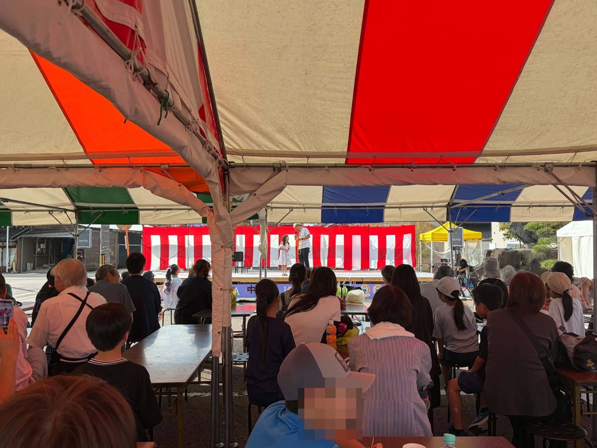 高岡市中田かかし祭の客席テントから、来場者と一緒に進めるマジックショーを見る様子