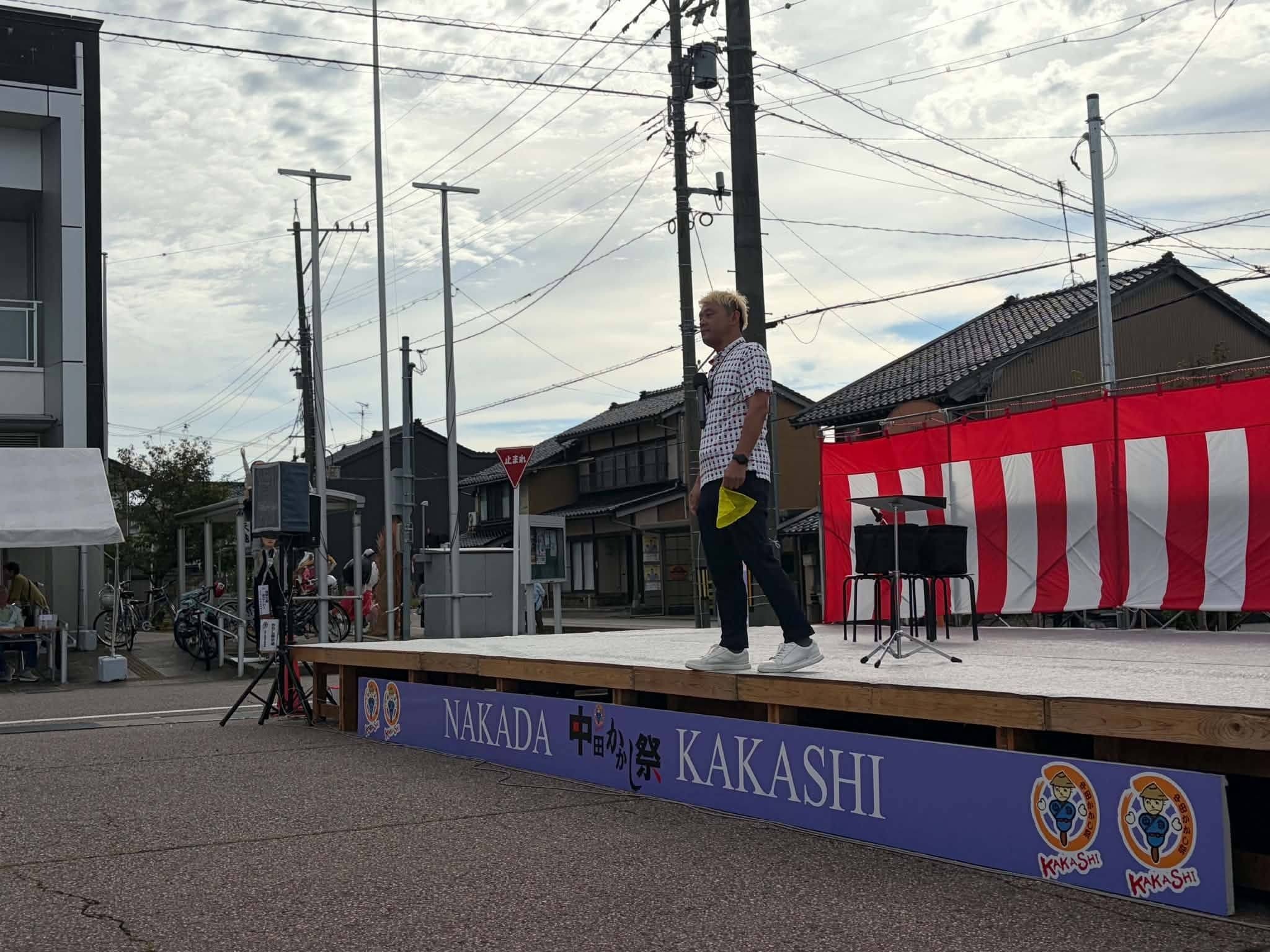 高岡市中田かかし祭の屋外ステージで黄色いシルクを手に話すマジシャン・コンプレッサー