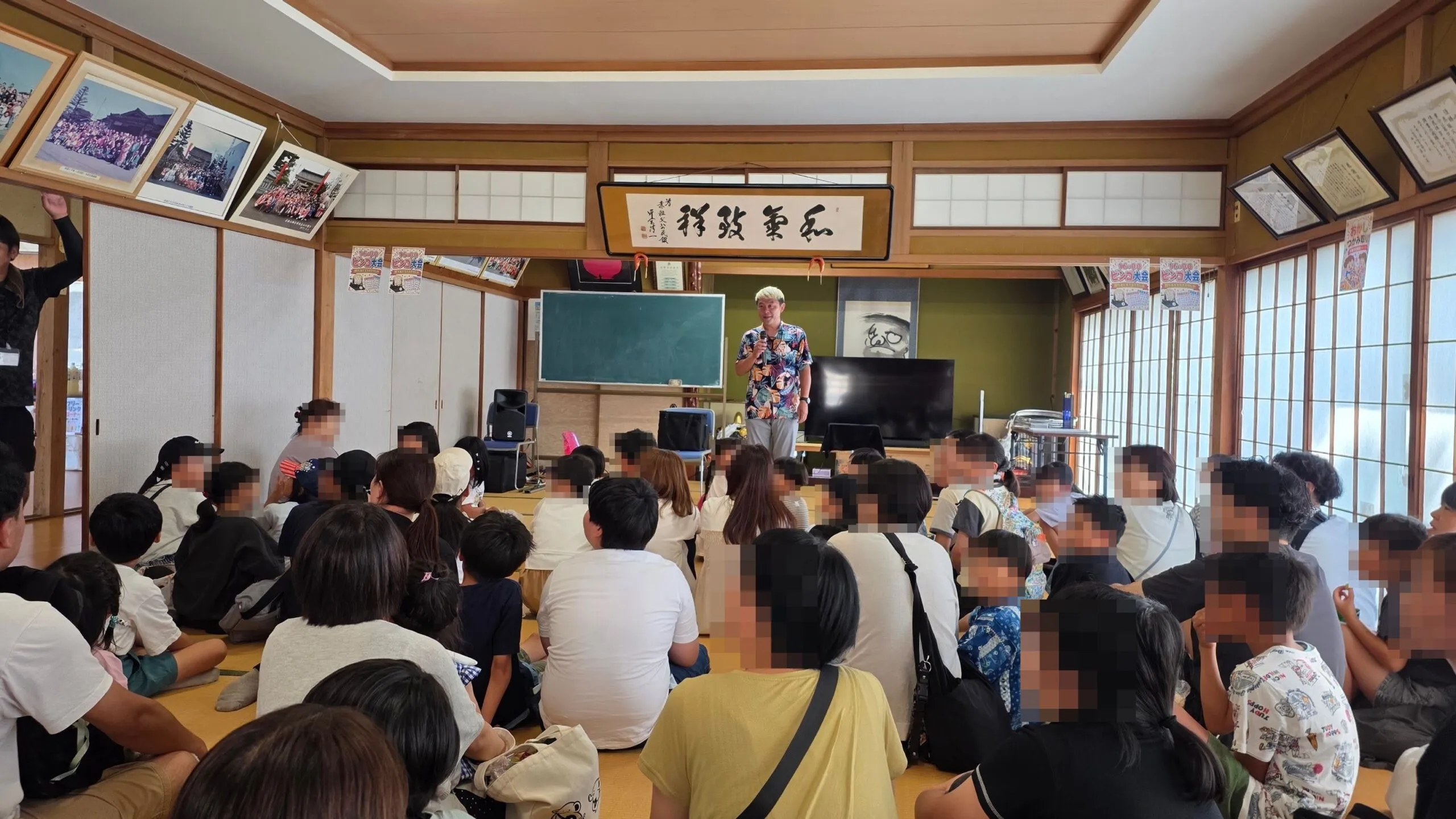 畳の部屋いっぱいに集まった子どもと大人の前でマジックショーを進めるマジシャン・コンプレッサー