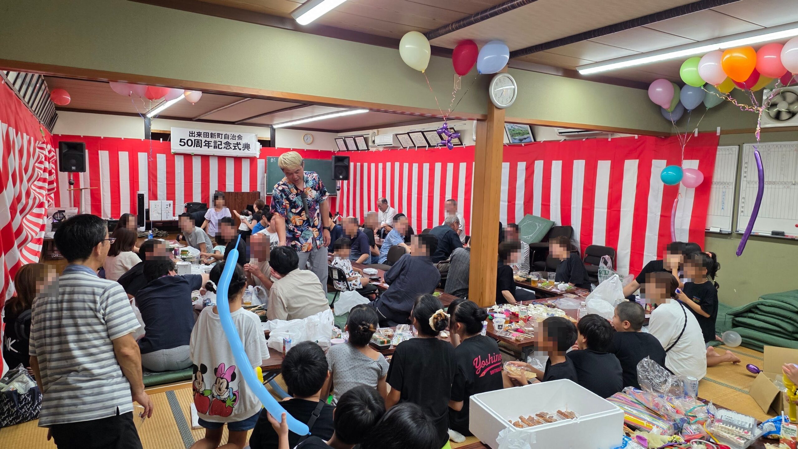 高岡市の納涼祭でマジックショー|50周年のお祝いと懐かしい再会 2 紅白幕と風船で飾られた公民館で観客の近くに立つコンプレッサー