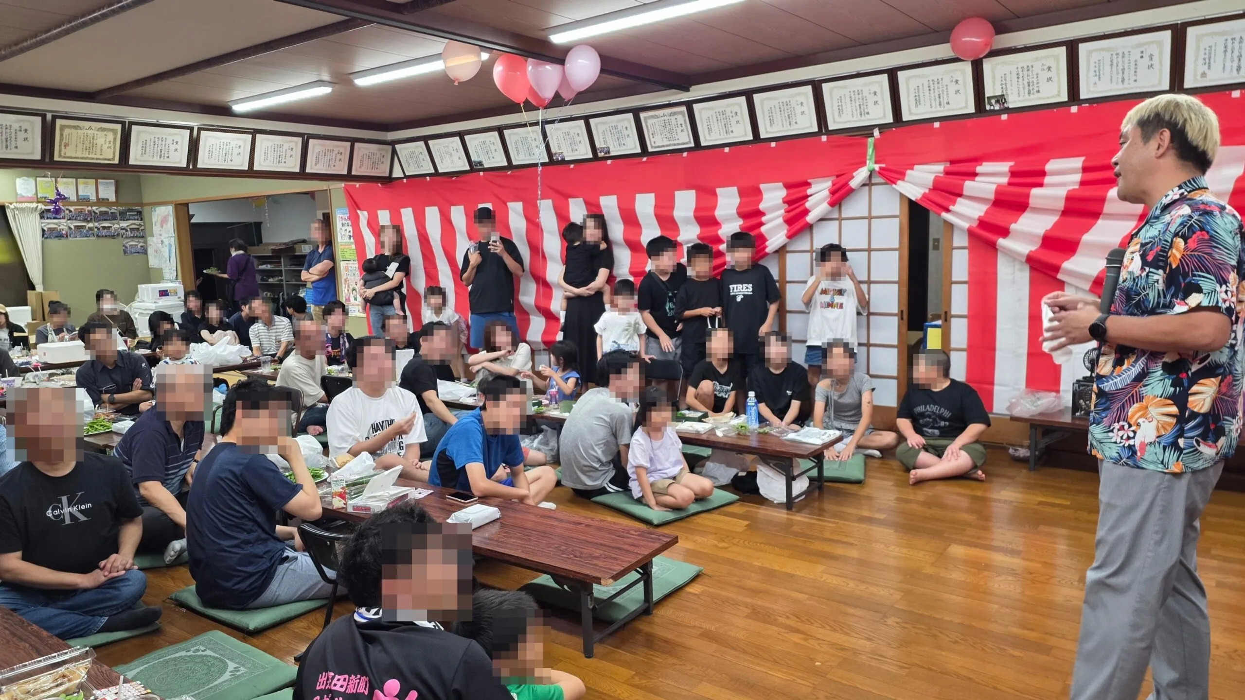 公民館の室内でマジックを披露するコンプレッサーを見守る子どもと大人たち