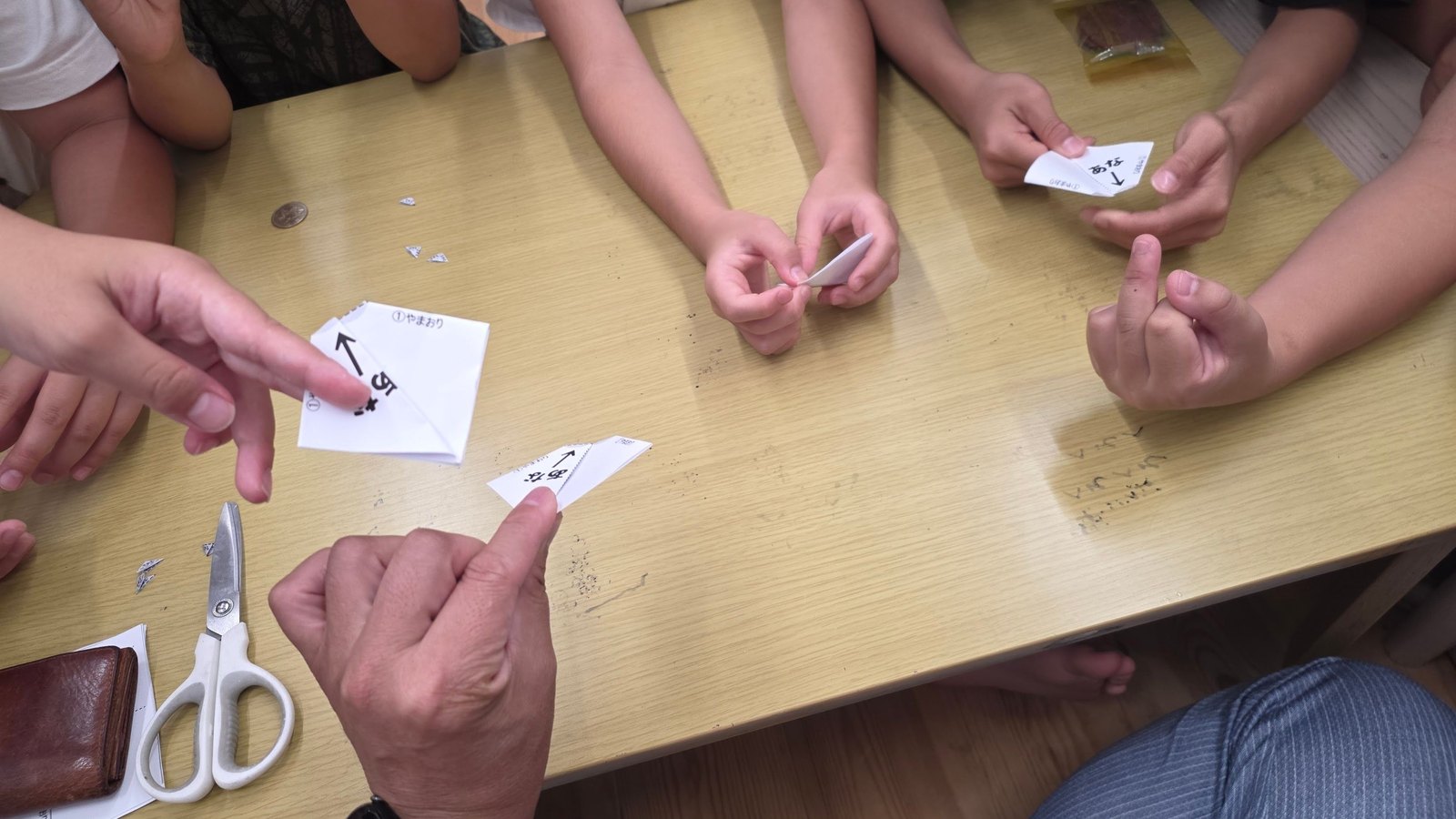1円玉サイズの穴を開けた紙とハサミ、手順が書かれた台紙を囲んで作業する子どもたちの手元