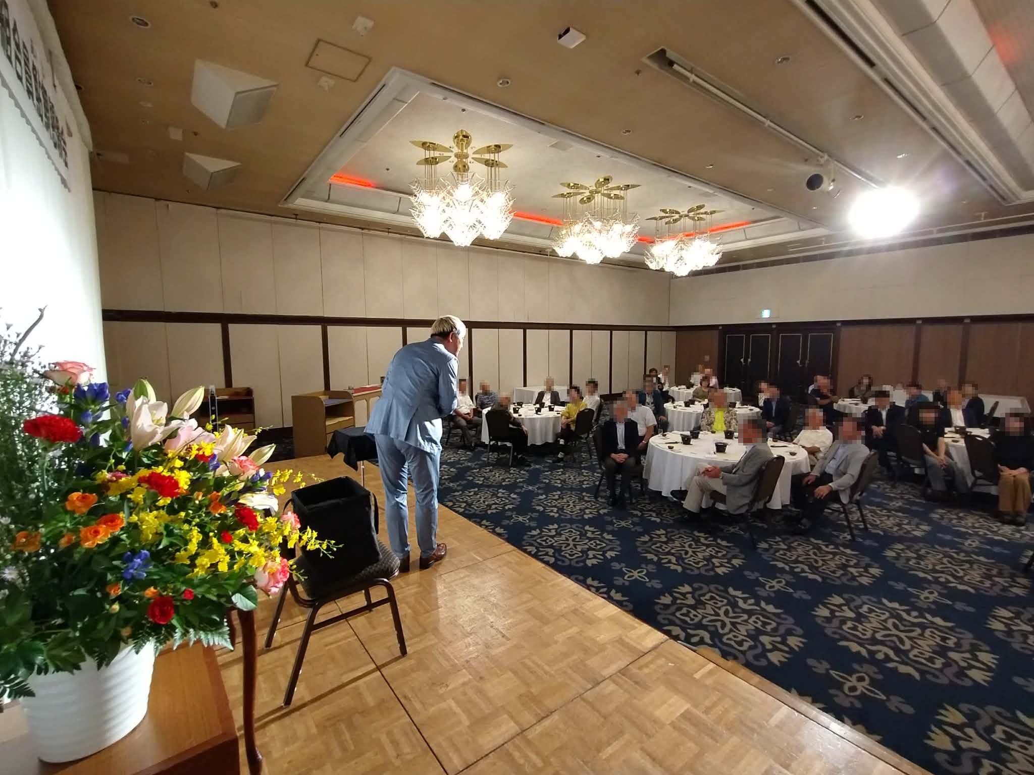 ホテルグランテラス富山のステージから客席へ身を乗り出し、鮎鯛懇親会の参加者と会話するマジシャン・コンプレッサー