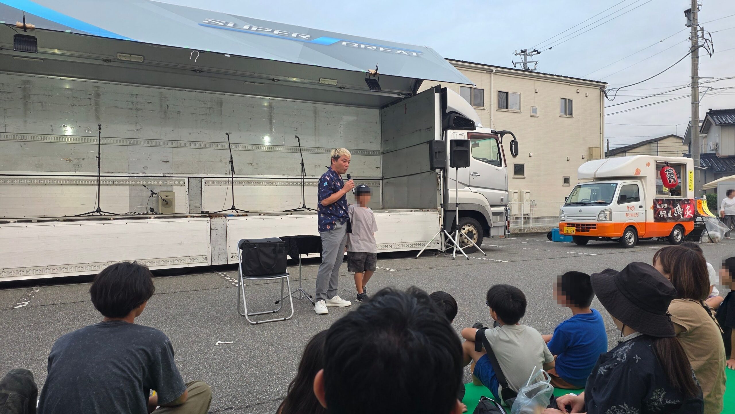 富山市の屋外マジックショーで、参加した子どもの横に立つコンプレッサーと見守る観客