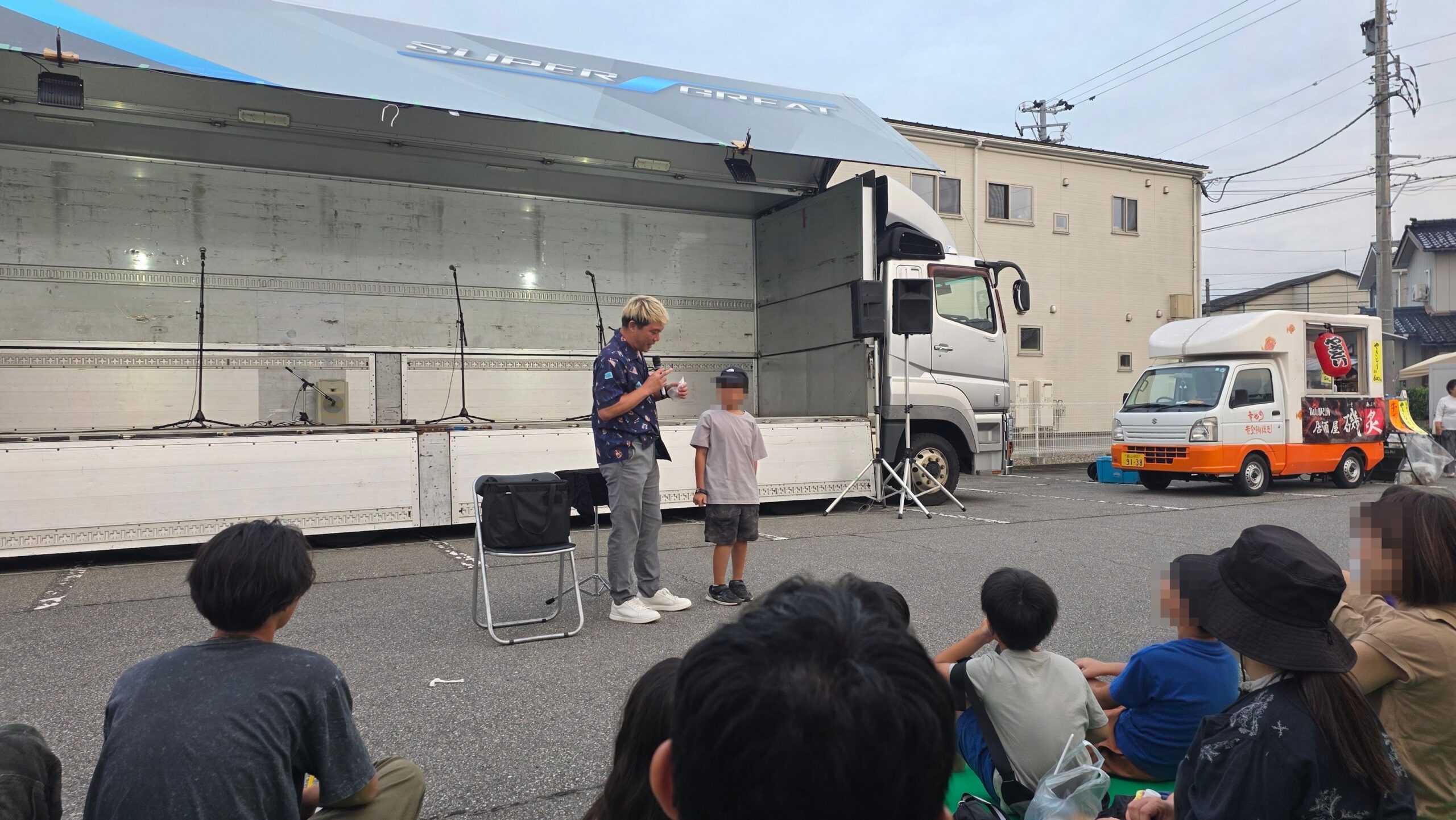 富山市の夏祭りで、白い道具を手にした子どもの隣でマイクを持つコンプレッサー