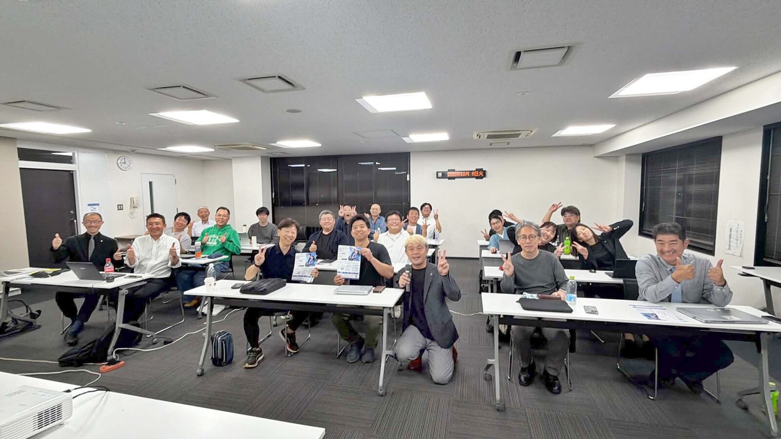 AIエージェント講座の終わりに撮った記念写真。会議室でピースサインや親指を立てて笑う参加者の皆さんと、前列中央のコンプレッサー