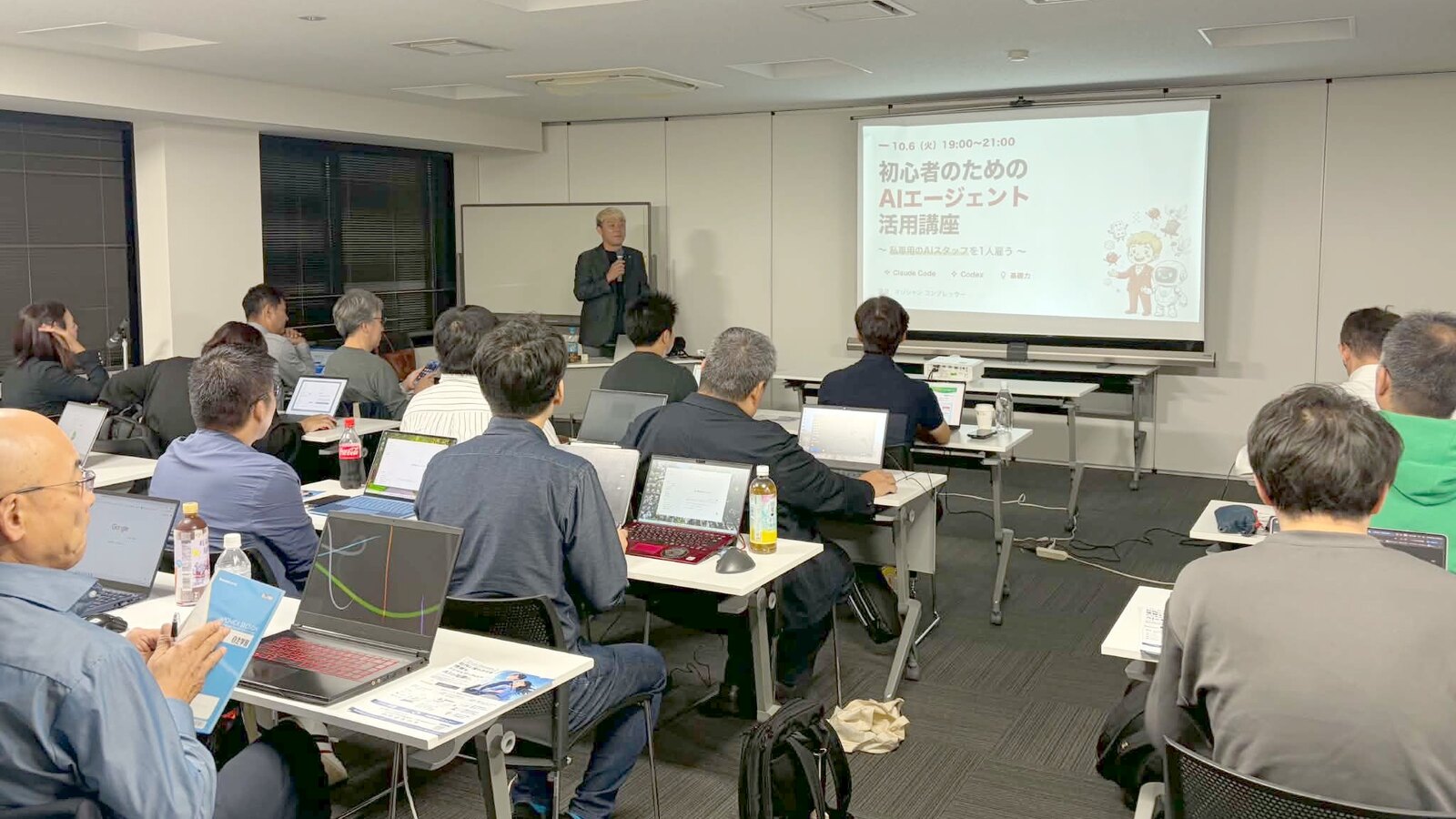 射水市で開いたAIエージェント講座で、スクリーンの横に立って話すコンプレッサーと、ノートパソコンを開いて聞く参加者の皆さん
