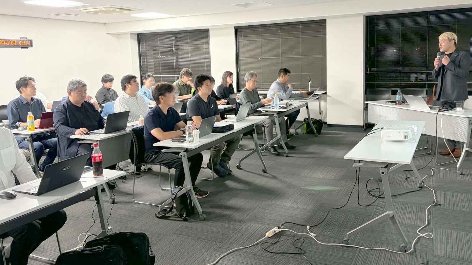 AIエージェント講座の前半、マイクを持って話すコンプレッサーと、机にノートパソコンを並べて聞く参加者の皆さん