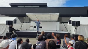 朝日町のひすい野ホール前の屋外ステージでマジックショーをするコンプレッサーと、手を挙げて応える客席の子どもたち