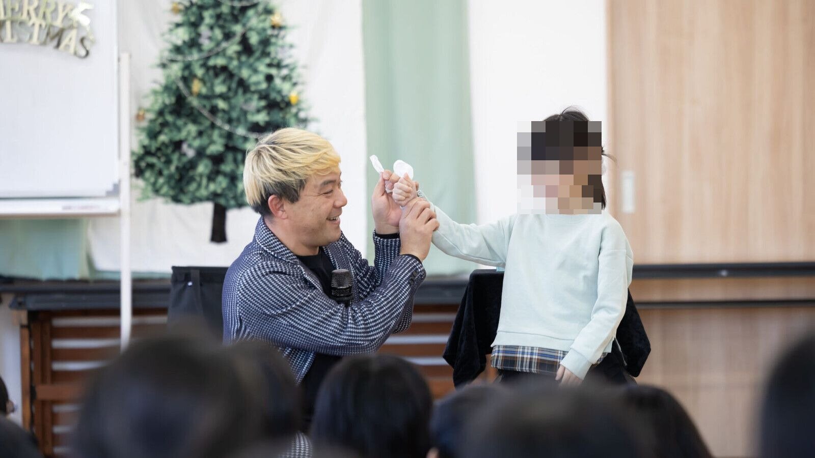子どものクリスマス会のマジックショーで、クリスマスツリーの前でお手伝いの女の子と一緒にマジックをするコンプレッサー（富山市の児童クラブ）