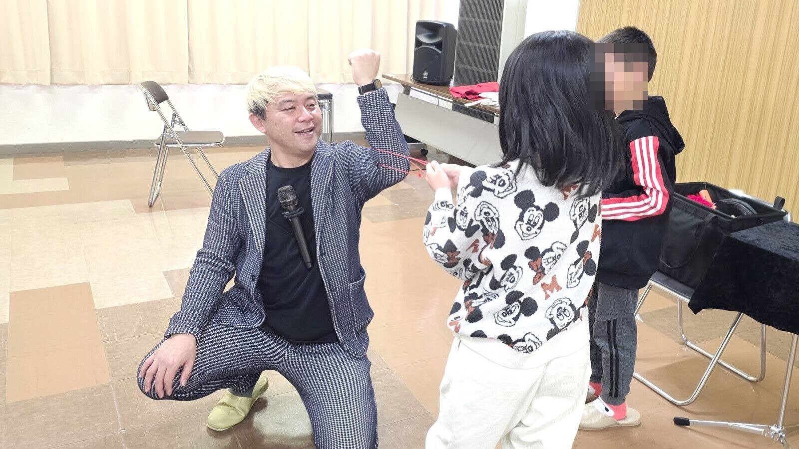 マジック教室の時間に、子どもと向き合って赤いひものマジックをやってみせるコンプレッサー（児童クラブ）