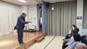 小矢部市の若林公民館で開催、いきいきサロンで約45分のマジックショー! 3 小矢部市の若林公民館のいきいきサロンで、ステージの端からいちばん前のお客さまに話しかけるコンプレッサー