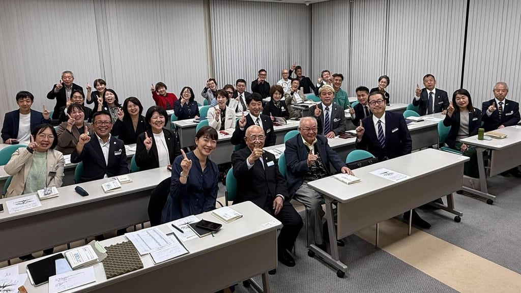 七つの原理勉強会の会場で、長机の席についた参加者が笑顔でカメラに向かう集合写真