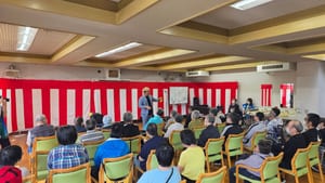 高岡市の障害者支援施設、志貴野苑の志貴野苑祭で、紅白幕の前に立ち黄色いハンカチを手に客席へ話しかけるコンプレッサー