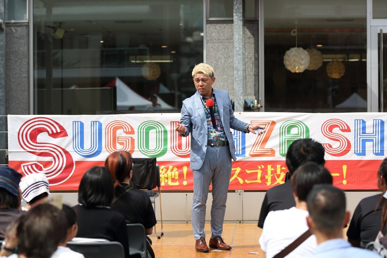 SUGOWAZA SHOWの横断幕の前で、客席に語りかけるマジシャン・コンプレッサー