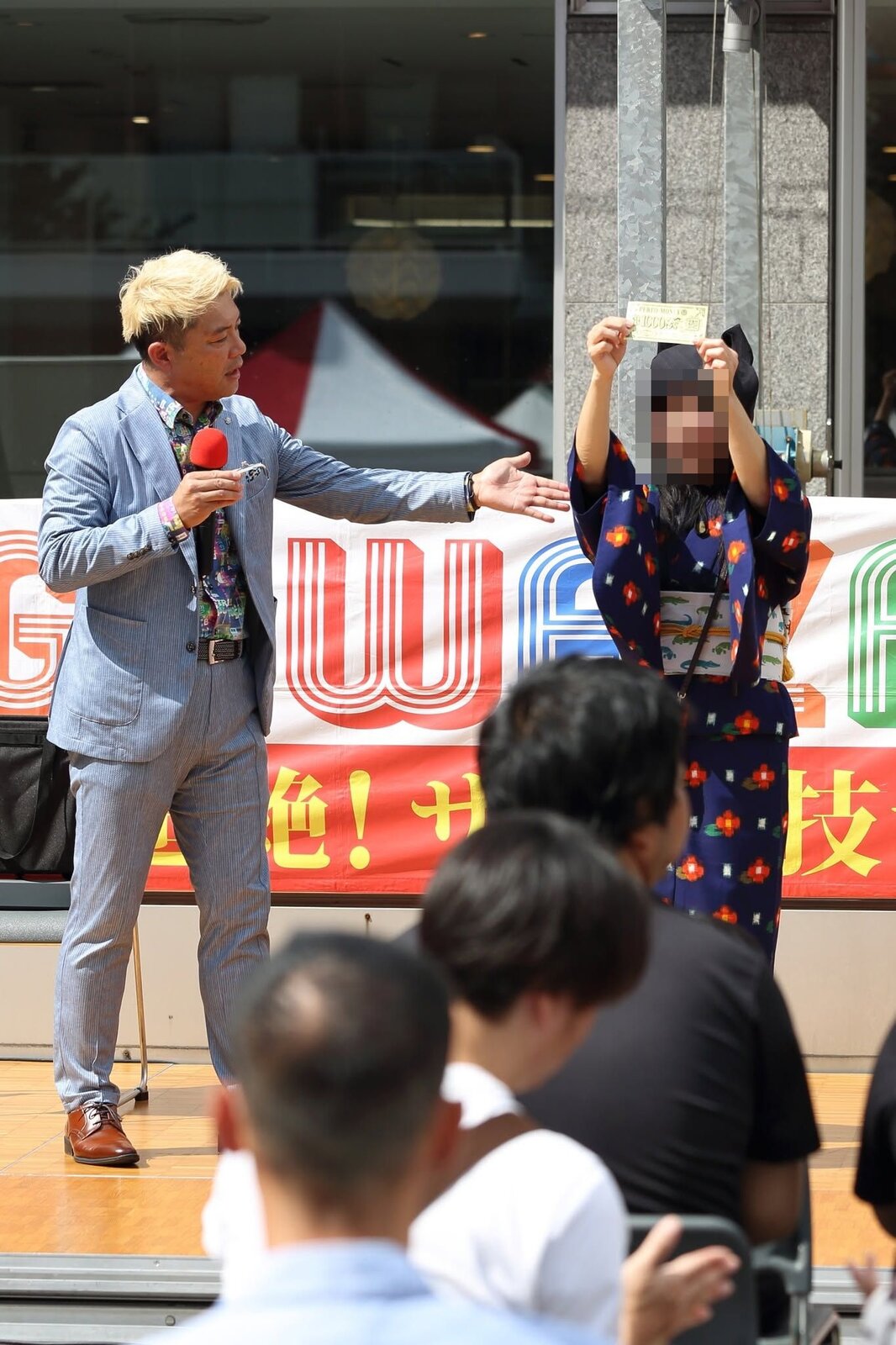お手伝いのお礼に受け取ったパフォマネーを客席に掲げて見せるお客さんと、マジシャン・コンプレッサー