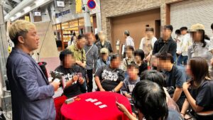 富山市総曲輪通りのスゴ技ストリートで、赤いテーブルを囲むお客さんにトランプのマジックを見せるマジシャン・コンプレッサー