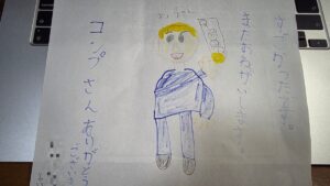 スゴ技ストリートで男の子からもらったプレゼント。金色の髪でトランプを掲げるコンプさんの絵と「すごかったです。またおねがいします。」の文字