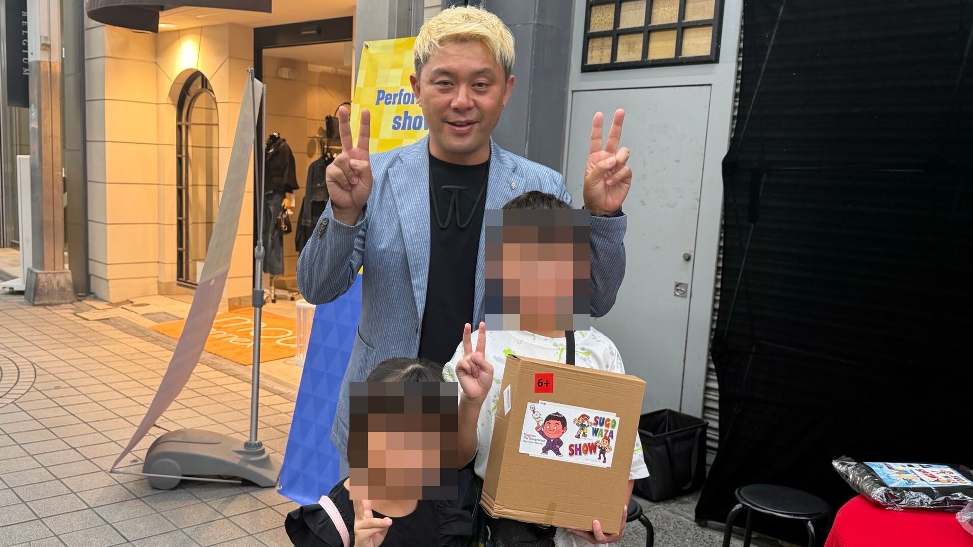 スゴ技ストリートでパフォマネー30枚と交換したマジックグッズの箱を持つ男の子と妹さん、ピースするマジシャン・コンプレッサー