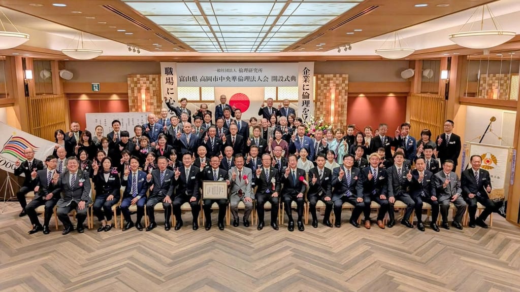 「富山県 高岡市中央準倫理法人会 開設式典」の看板と日の丸を背に、前列中央に認可書の額を掲げ、会員と来賓が並んだ集合写真