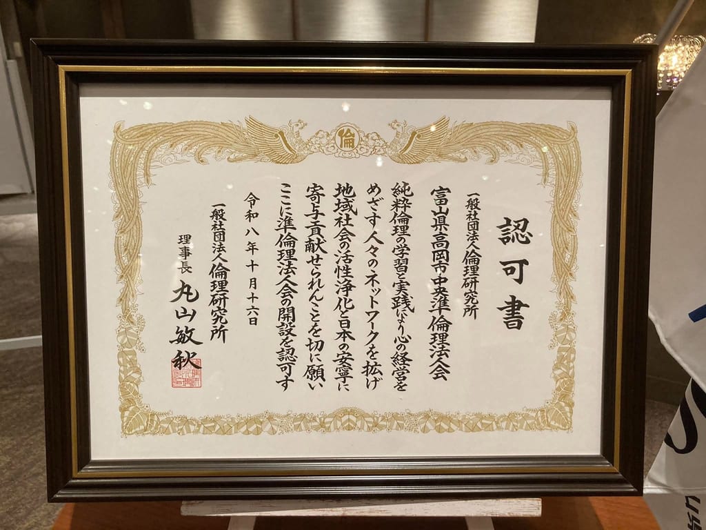「富山県高岡市中央準倫理法人会」の開設を認可すると書かれ、令和八年十月十六日の日付が入った、金色の鳳凰の飾り枠の認可書