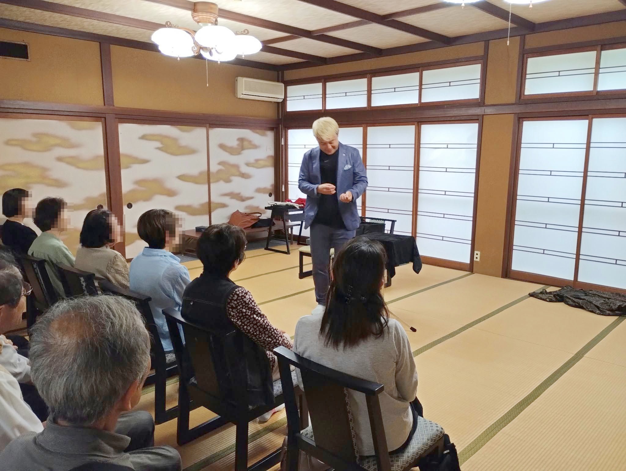 町内会の合同マジックショーで、手元を見つめながら演技を進めるコンプレッサーと、見守るお客さま