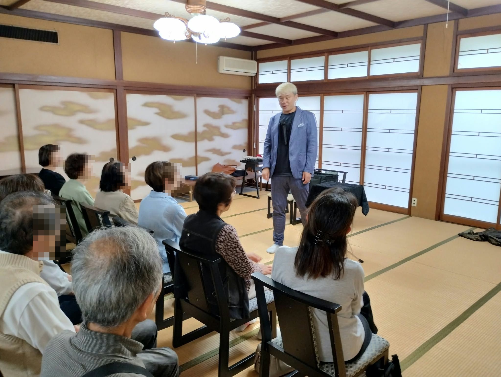 高岡市福岡町のマジックショーで、和室に並んだ椅子席のお客さまに語りかけるマジシャン・コンプレッサー