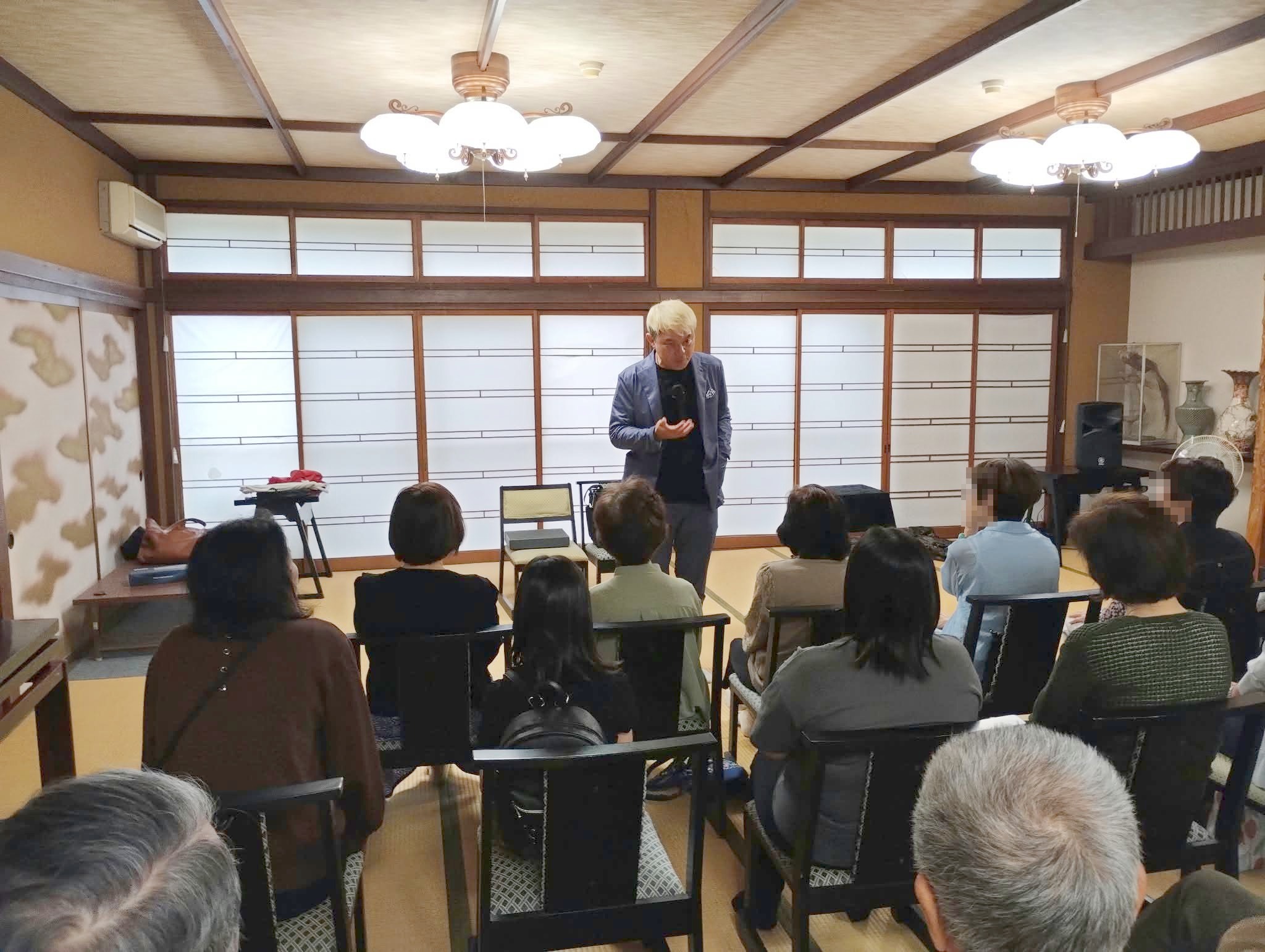 椅子席のお客さまのすぐ前で、手のひらを差し出して語りかけるコンプレッサー