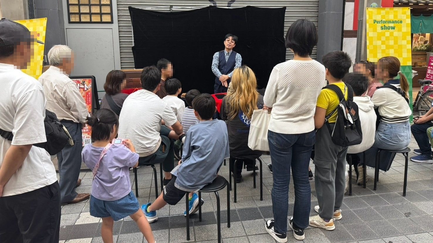 富山市総曲輪通りのストリートショー「スゴ技ストリート」で、椅子に座った子どもたちや立ち見のお客さまにマジックを見せる所属マジシャンのマーサ