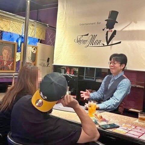 富山市桜木町のマジックバーのカウンターで、お客さまおふたりに両手を広げて話しかける所属マジシャンのマーサ