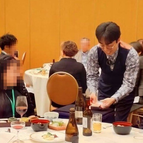 懇親会のテーブルで、お客さまの前に身をかがめて手元のマジックを見せる所属マジシャンのマーサ