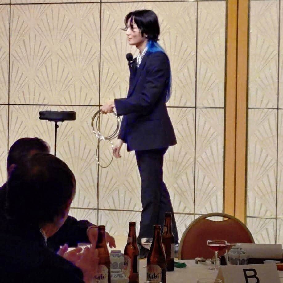 ホテルの宴会場のステージで、銀色のリングを手にマジックを見せる所属マジシャンのよぉすけ
